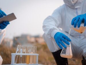 Scientists in full PPE collecting water samples outdoors. PFAS Groundwater contamination. PFAS in Dry cleaning.